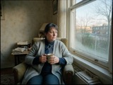 An adult sitting by a window with a mug, looking outside