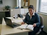 An adult at an office desk with a notebook and a laptop
