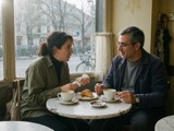 Two adults talking over coffee at a cafe table