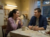 A married couple talking at a kitchen table over coffee