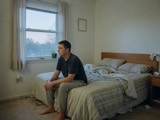 An adult sitting on the edge of a bed at dawn, looking toward a window