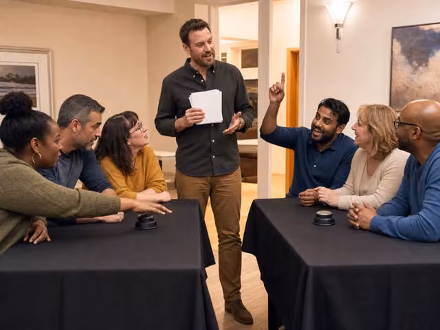 A standing host holding a card while two groups sit across a table.