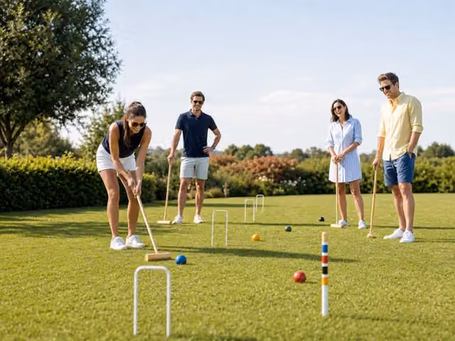 Friends with mallets playing croquet around balls and wire hoops on a lawn.