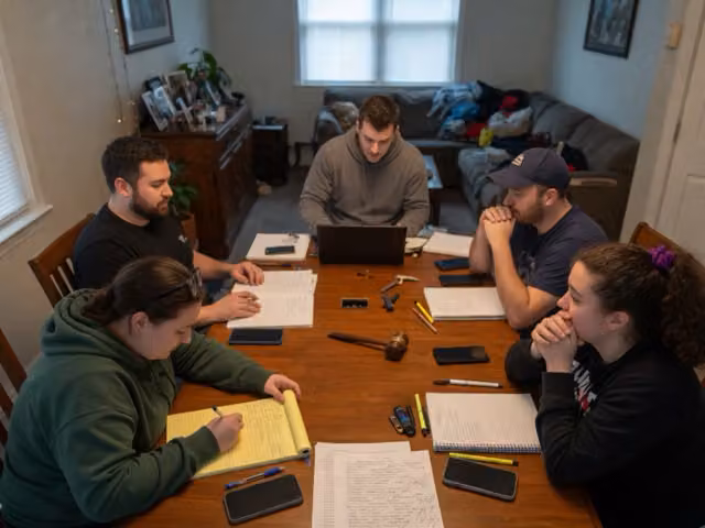 Friends seated around a table with notebooks during a fantasy draft.