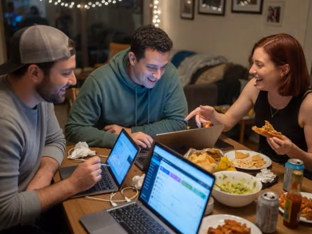 Friends checking laptops together at a table during a fantasy draft.