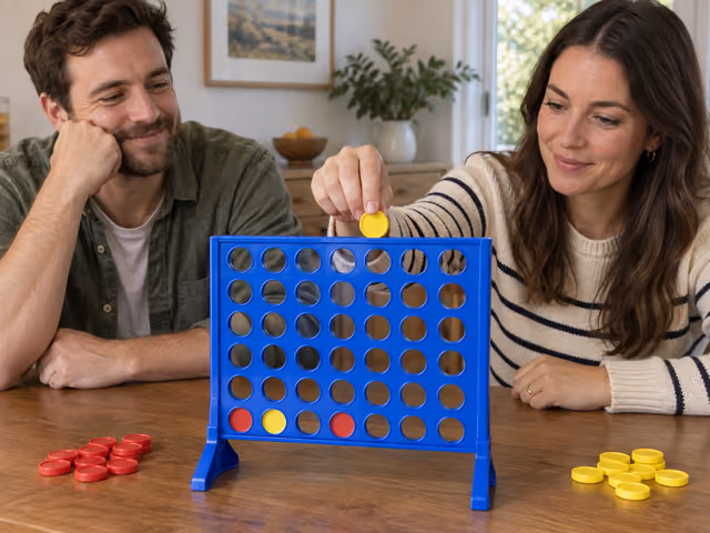 Two adults playing Connect Four with red and yellow discs in a blue rack