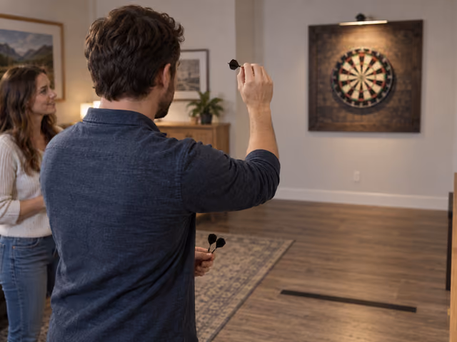 A darts player aiming toward the board while another adult watches from behind