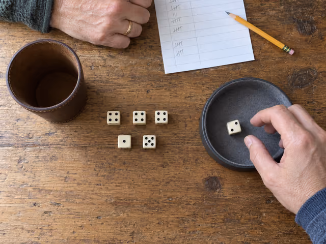 A hand prepares to reroll one die beside five scoring dice in Farkle