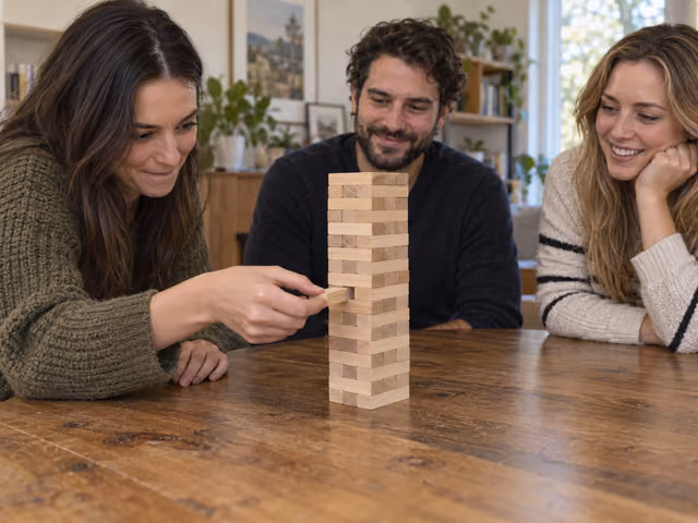 Three adults watching a player remove one wooden block from a Jenga tower