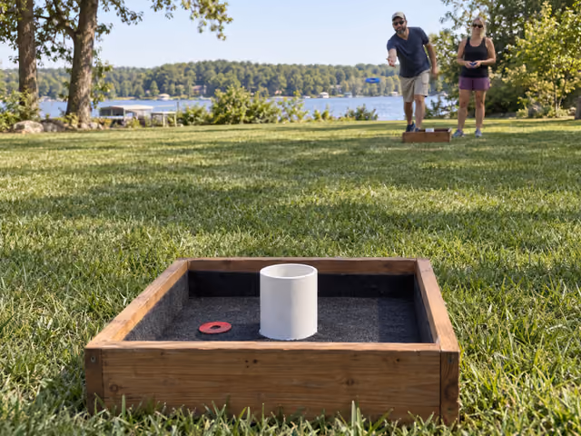 Two adults tossing washers toward a wooden box with a center cup