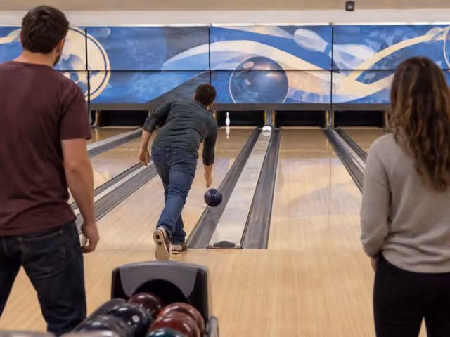An adult bowling toward one remaining pin during a spare attempt