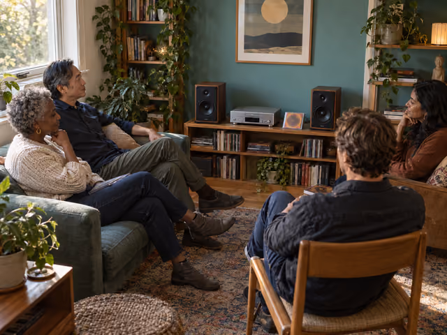 Four adults seated in a home music room facing a CD stereo and two bookshelf speakers.