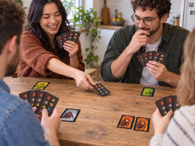 Four adults demonstrating a face-down Cockroach Poker pass with separate face-up creature cards on the table.