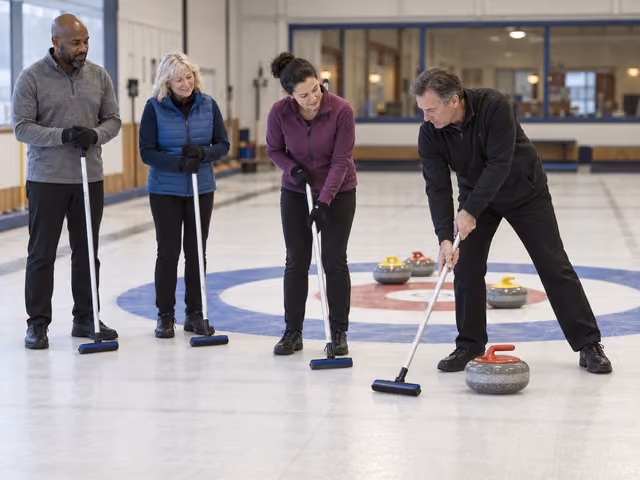 An instructor demonstrates broom use beside a curling stone while three adults watch on an indoor curling sheet.