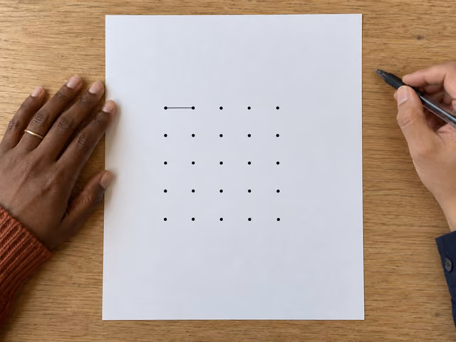 Two players' hands beside a paper Dots and boxes grid with its first horizontal line drawn.