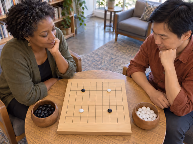 Two adults studying four black and white stones on a small wooden Go board, with bowls of spare stones beside it.
