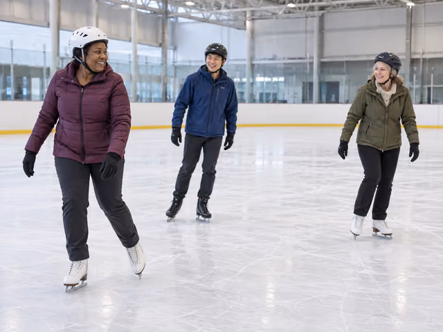 Three adults in helmets and gloves glide separately on figure skates across an indoor ice rink.