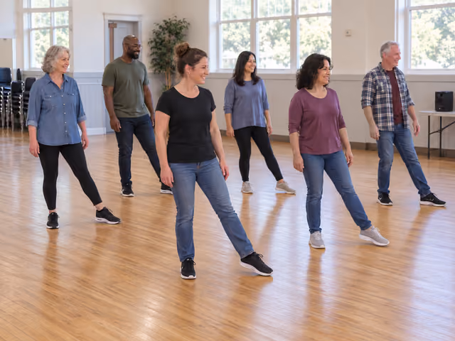 Six adults in staggered rows practicing a coordinated line-dance step on a clear wooden community-hall floor.