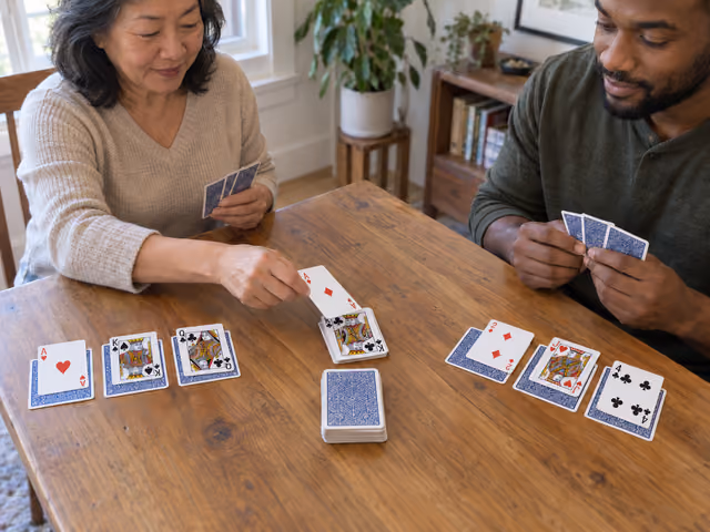 Two adults playing Palace with exposed playing cards above three hidden cards per player and separate central draw and play piles.