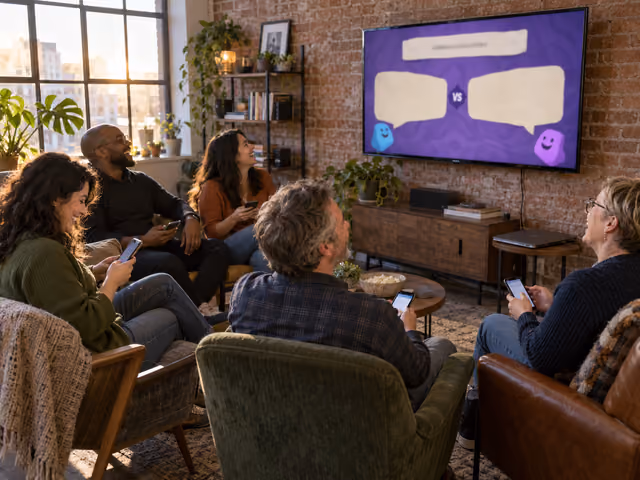Five adults holding separate phones while watching a shared screen with two answer panels in a sunlit loft.