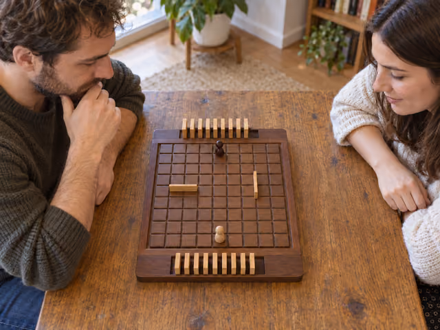 Two adults study a wooden Quoridor board with two pawns, two placed walls and separate wall reserves.