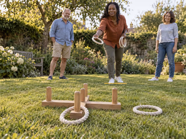 Three adults playing lawn ring toss with rope rings and a low five-peg wooden target.