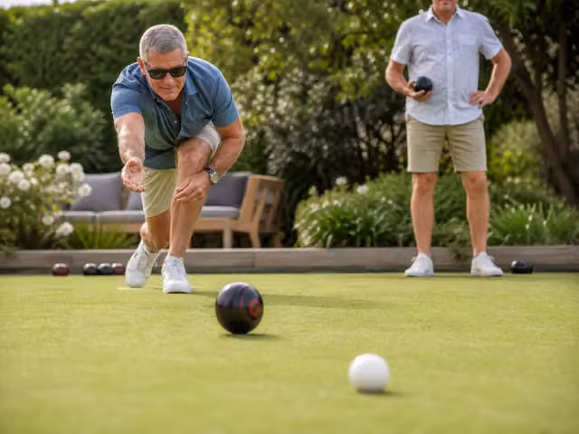 An adult delivering a biased bowl toward a white jack on a maintained outdoor bowls green.