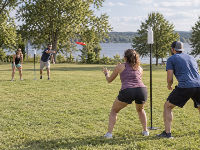 Adults tossing a disc toward a freestanding pole topped by a bottle.