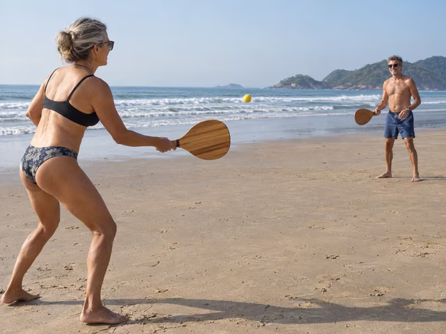 Two adults rallying with wooden paddles on a beach.